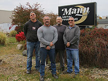Four Men Standing in front of Mann Metal Sign Smiling