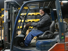 Guy with glasses smiling in flannel Jacket on grey and orange forktruck