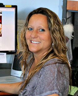 Tammy Ackerman Hr Manager wearing grey shirt at desk with computer smiling at work