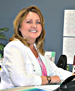 Tammy Collins Ceo sitting at desk in white jacket smiling at work