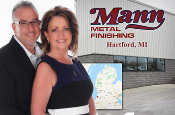 Owners Tammy and Greg posing with Mann Logo Building and Map
